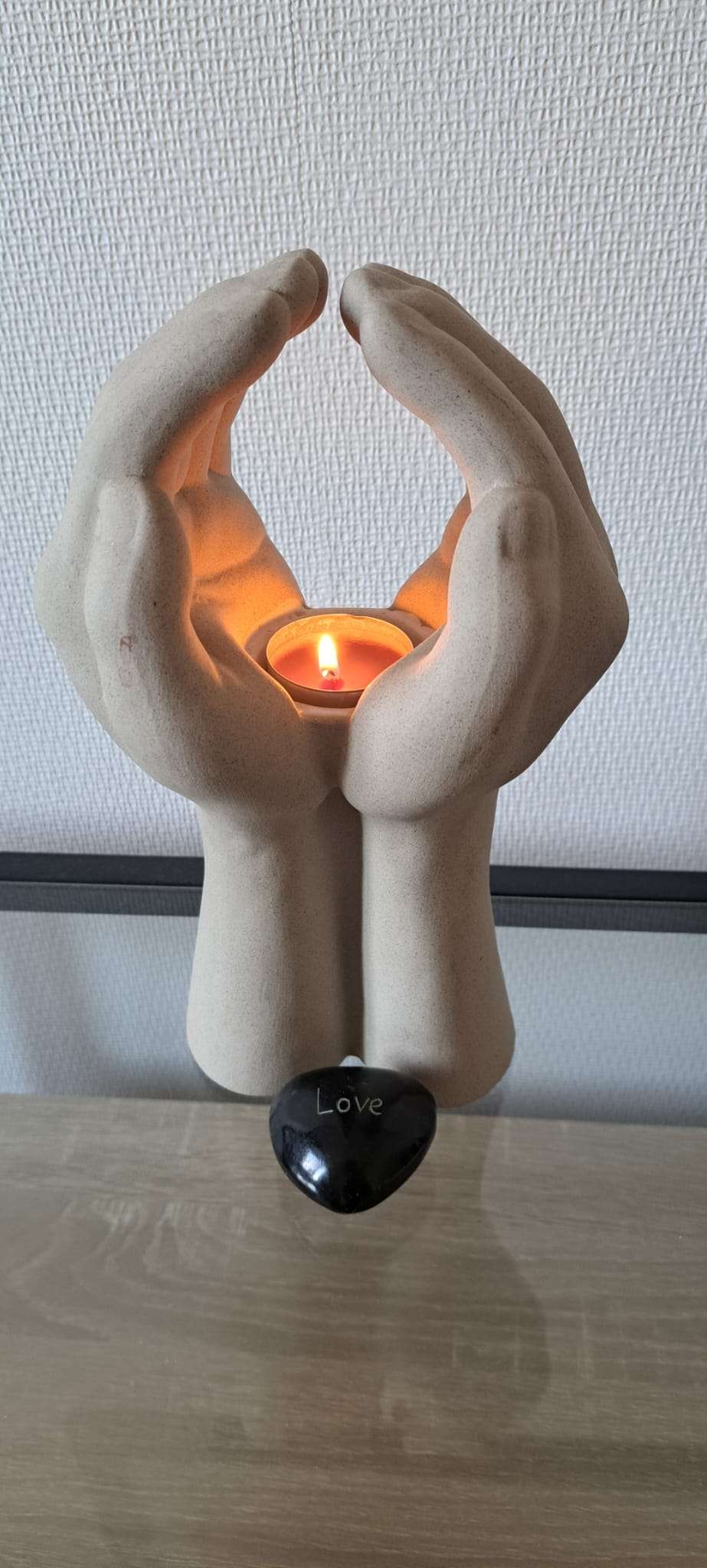 Brandend kaarsje in handen met steentje met tekst 'Love'